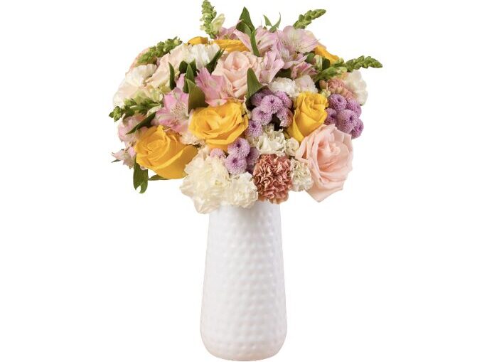 Bouquet of yellow roses and pink, white, and purple flowers in a tall white textured ceramic vase.