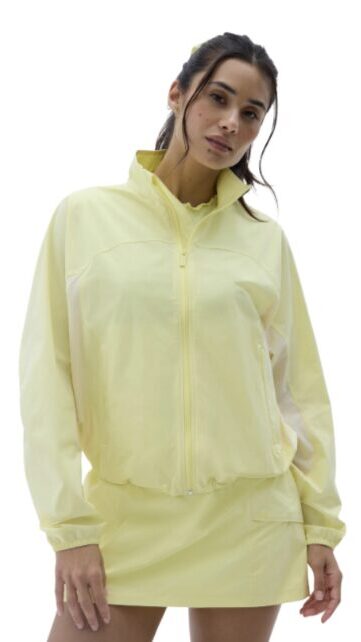 Woman in a pale yellow zip-front windbreaker with a matching mini skirt, posing against a white background.