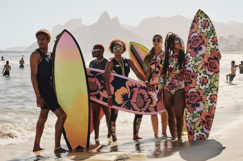 Farm Rio Rip Curl surf collection group of riders with floral print boards on the beach