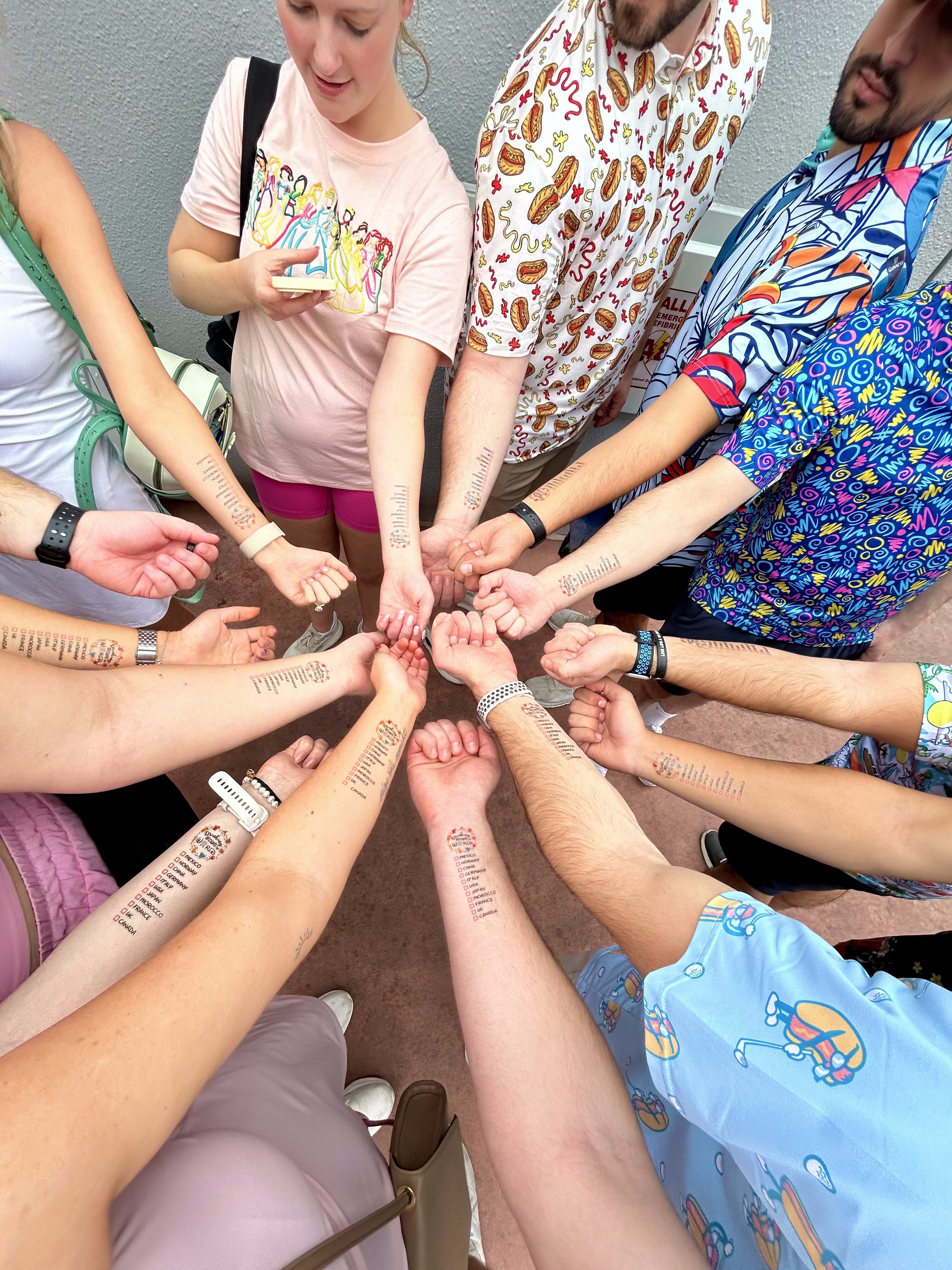 Group of people standing in a circle, showing forearm tattoo tests or stamps on each arm close together in a communal gesture.