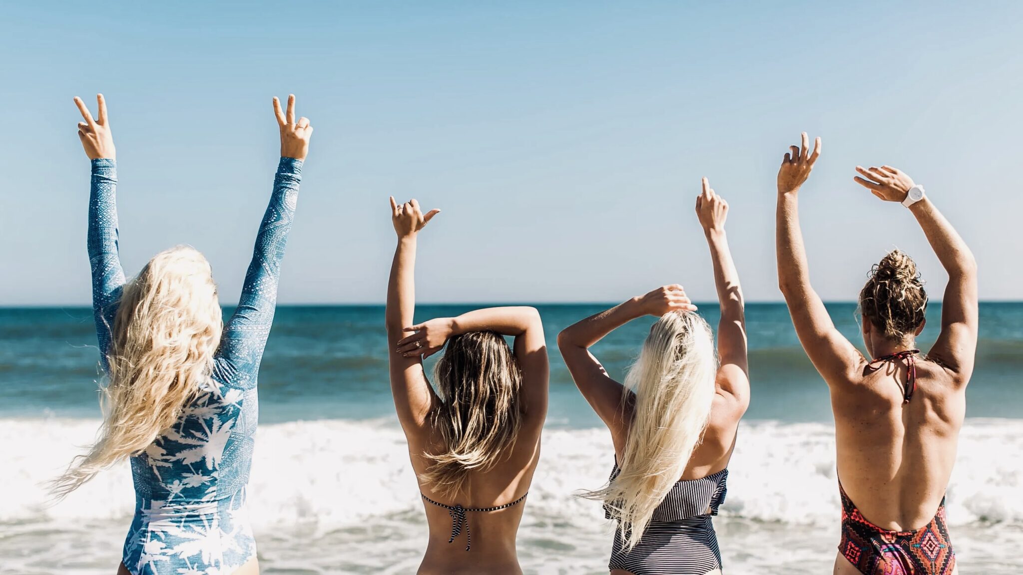 Four women with saltwater hair on the beach with arms raised