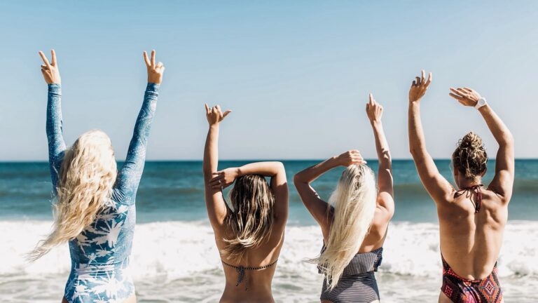 Group of friends with saltwater hair, arms raised on a sunny beach