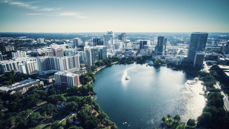 Aerial view of a downtown city surrounding a circular lake with a fountain and green park spaces.