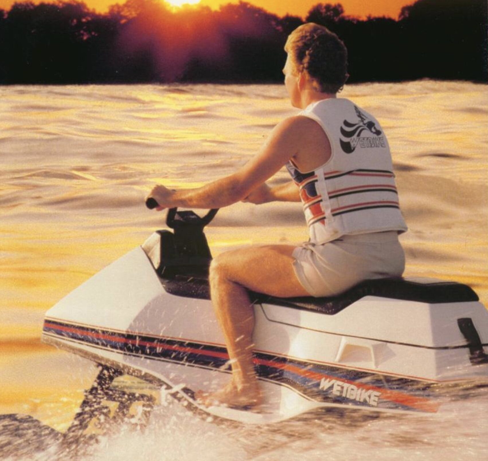 Person riding a white and red jet ski on the water at sunset, back to the camera, wearing a white striped tank top.",