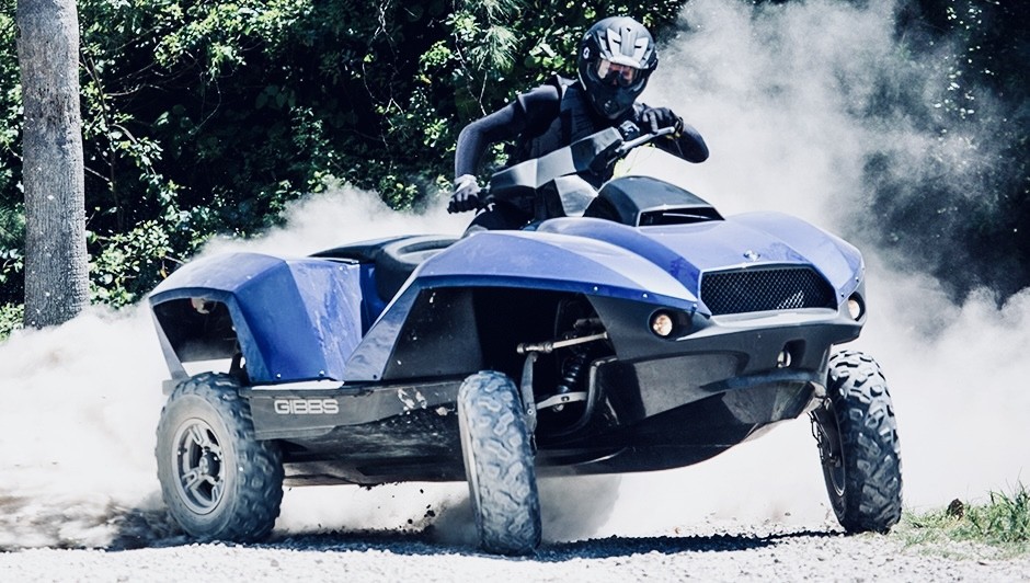 0ab6d00a-f5f0-4c87-9a57-f6f657a47517 - The Wake Edit Rider wearing a helmet on a blue ATV kicking up dust on a dirt trail in a forested area.
