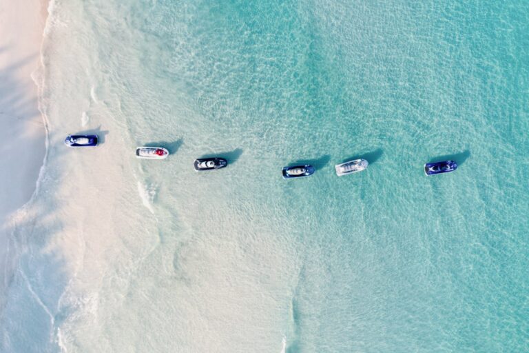 Overhead view of a turquoise ocean with several small boats near a pale sandy beach.