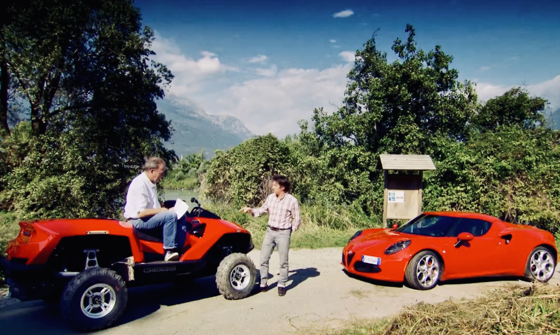 Screenshot - The Wake Edit Two men talking beside a red sports car and a red ATV on a dirt road, with trees and mountains in the background on a sunny day.
