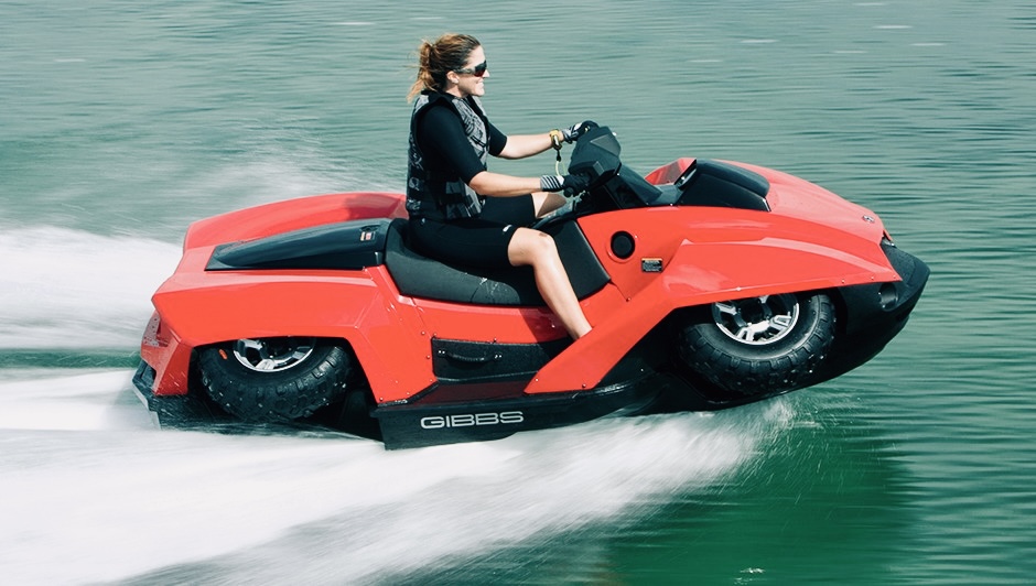 image 2 - The Wake Edit Person wearing life vest rides a bright red jet ski across blue-green water, spray at the rear, sunlight on water surface
