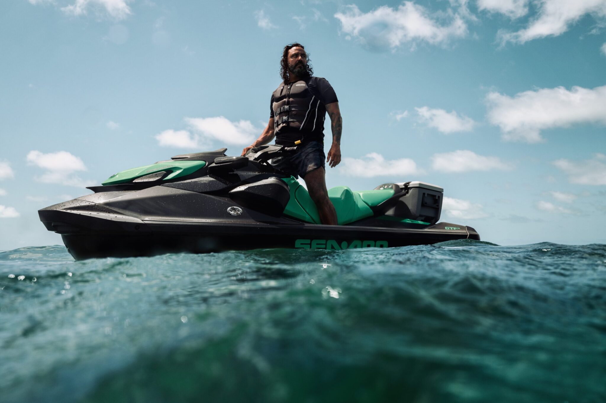 Image 1 - The Wake Edit Man standing on a green and black jet ski, wearing a life vest, on clear blue water under a sunny sky.