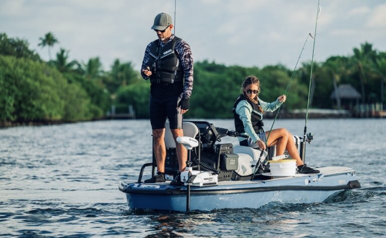 Two people fishing from a small blue boat on calm water, wearing life jackets and hats, with fishing rods raised.