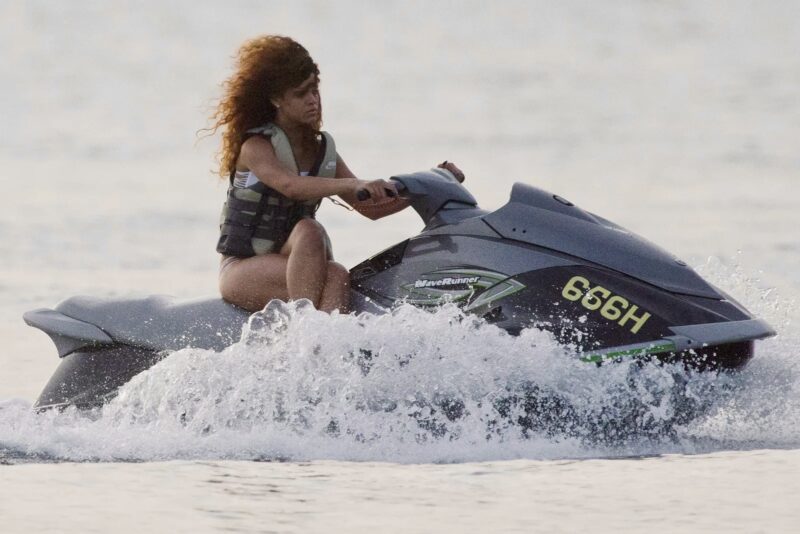 Rihanna sitting side-saddle on a jet ski in an understated swimwear look