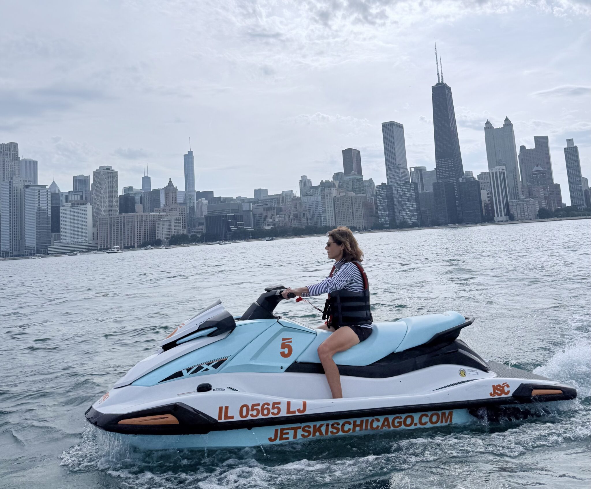 Image 1 - The Wake Edit Person riding a turquoise jet ski on a lake with the Chicago skyline in the background, wearing a life jacket.