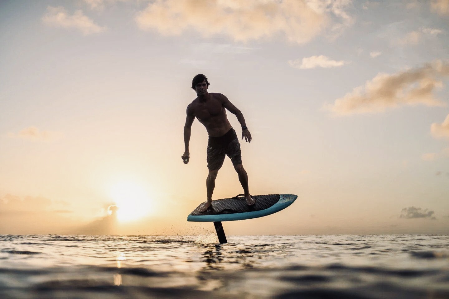 MAIN - The Wake Edit Man standing barefoot on a turquoise stand-up paddleboard, paddling on calm ocean at sunset.